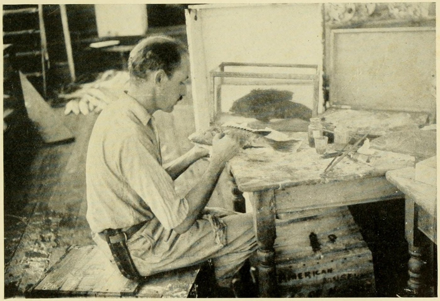 Dwight Franklin at a cluttered workbench, painting a model fish